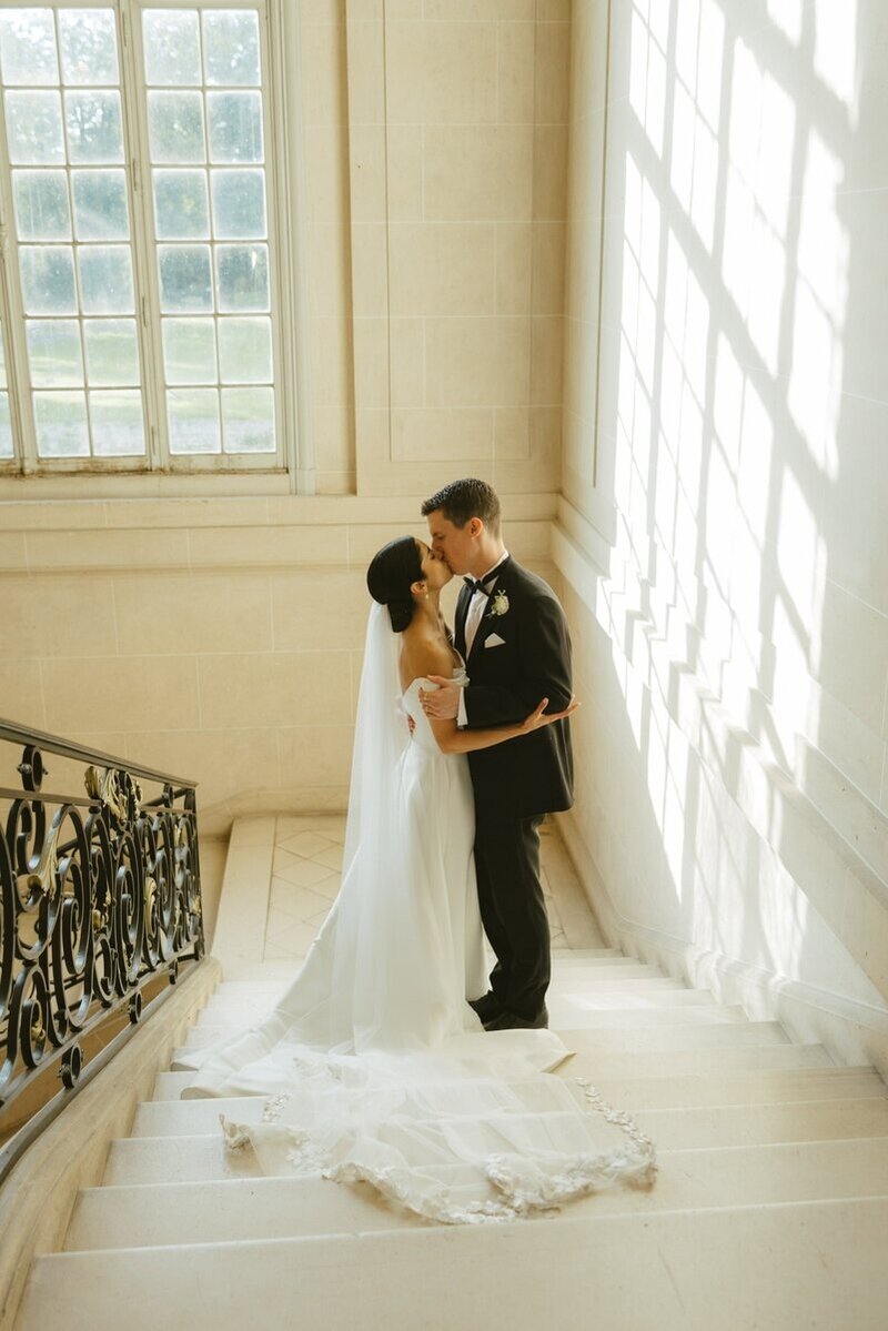 A bride and groom kissing on the steps of a historic chateau shot in an editorial photography style by Stacey Vandas Photography