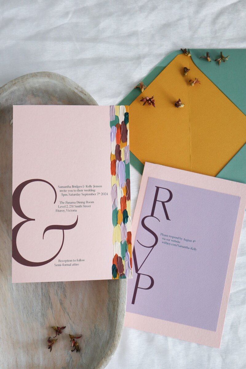 Painted wedding invitations with blush pink card, lilac RSVP card, and multiple paint colours.  The invitation has a large ampersand.