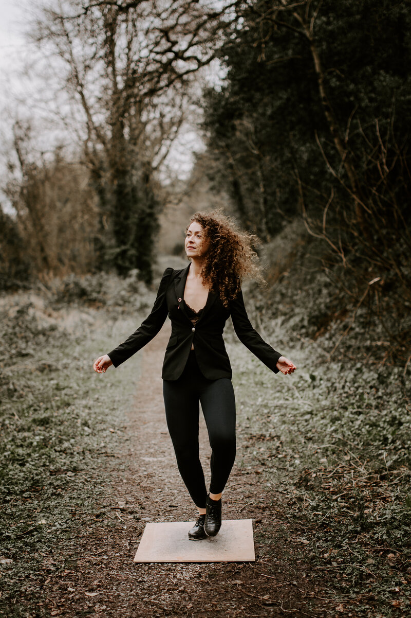 Seána Redmond in a reflective sean nós dance pose outdoors, looking to the right in a woodland setting, symbolising a connection to Irish heritage, music, and storytelling