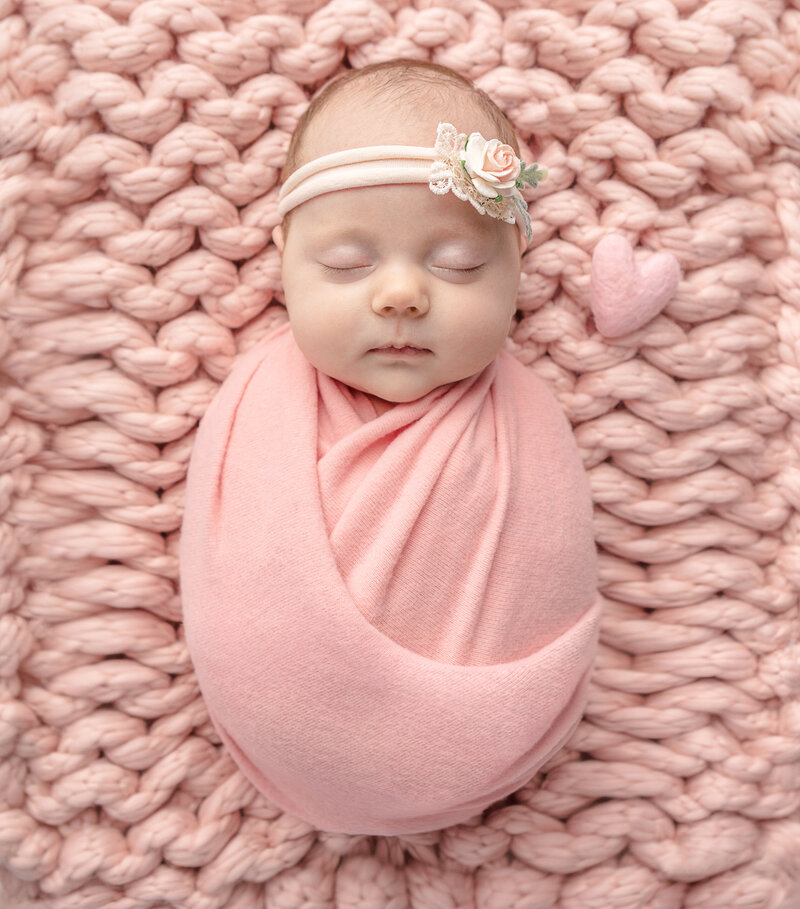 peaceful newborn portrait of a baby girl perfectly swaddled in peachy pink, sleeping on a chunky knit peachy pink blanket