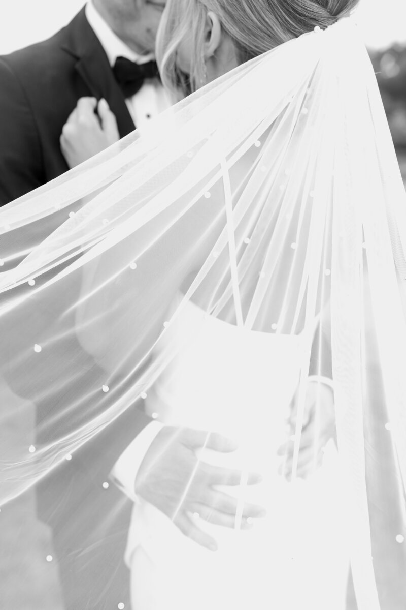 Bride and groom embrace as bride's veil blows in the breeze