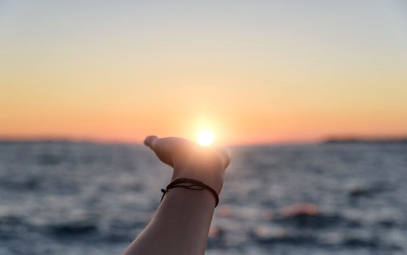 Woman's hand outstretched toward the sun as the light hovers in her palm