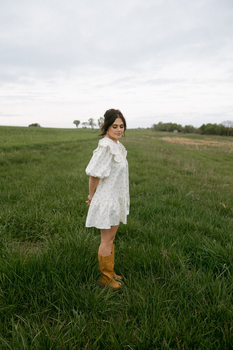 woman standing in an open Kansas field smiling softly while wearing a ruffled floral dress


