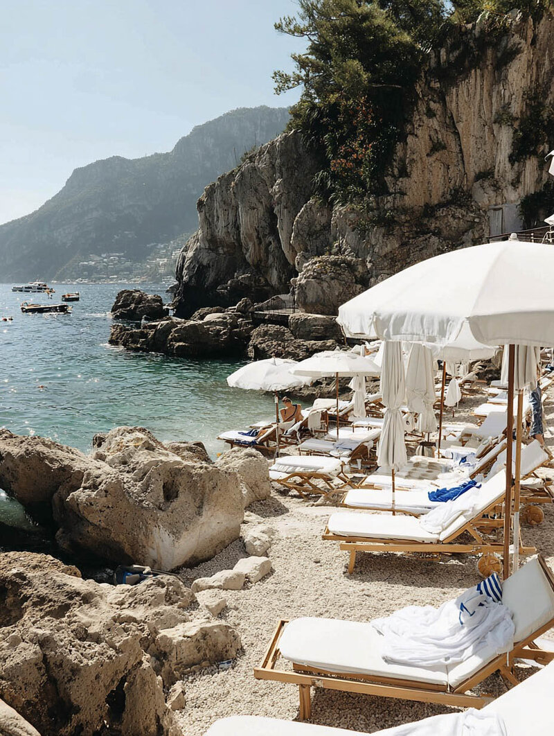 Vacation moment: white loungers under shade with expansive ocean views on a European rocky coast. Tailored Oasis Travel Co.
