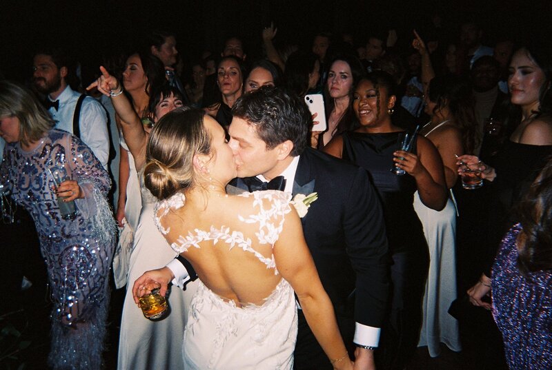 Flash photo of bride and groom kissing on the dance floor with guests behind them