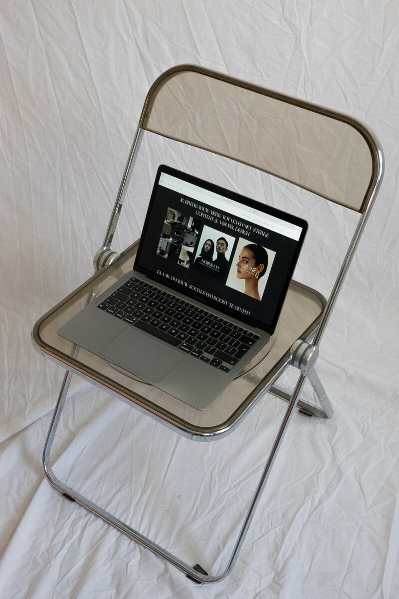 A laptop showing a custom Showit website page, standing on top of a plastic chair in a photo studio.