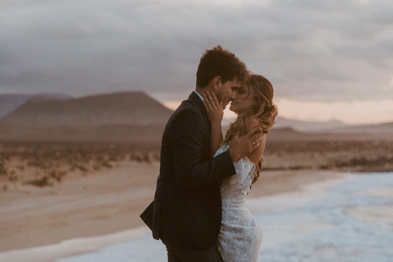 Bride and groom kissing on beach at sunset