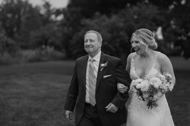 A father walking their child down the aisle as they both smile 