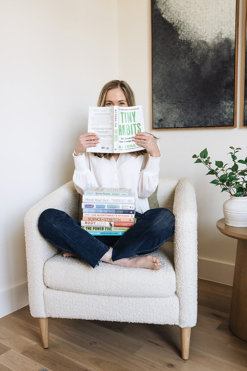 Erica Taylor sitting with wellness books and smiling behind ‘Tiny Habits’—offering a self-paced nutrition course for moms to gain clarity and confidence with food