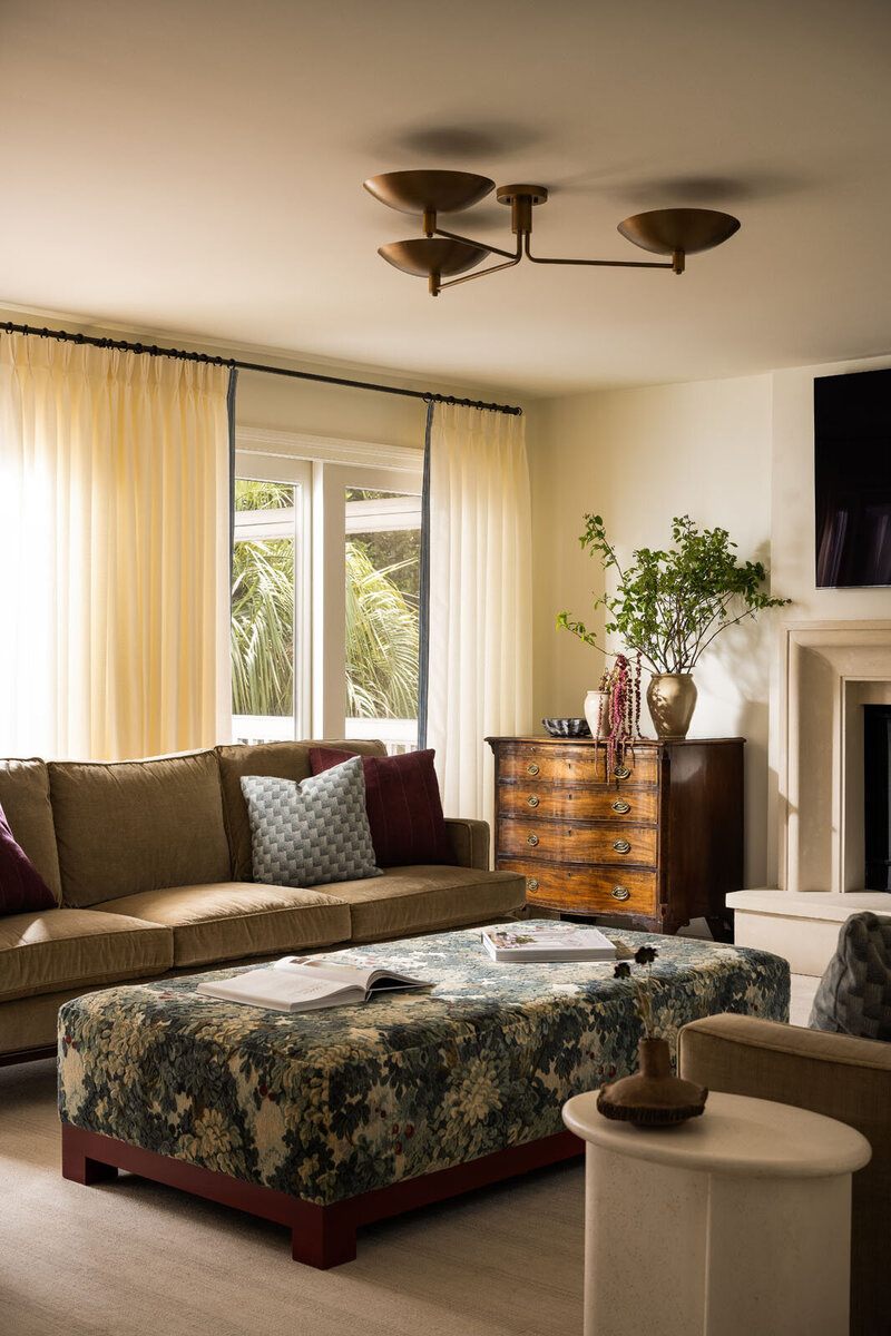 Bold living room with beige couches, green velvet ottoman and patterned artwork