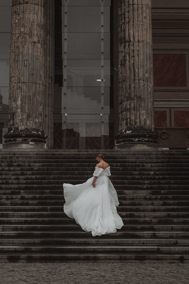 Brud fixar sin klänning på en trappa vid ett monument