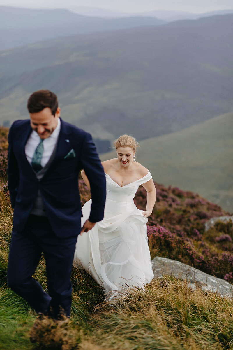 Bride and groom walking joyfully in wedding attire through the Wicklow Mountains after their ceremony, surrounded by wild heather and scenic views