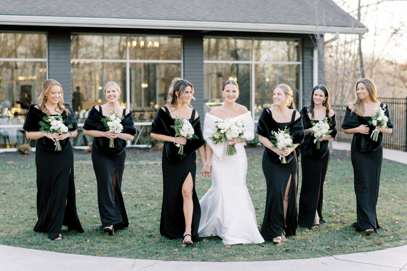 bride and bridesmaids in all black dresses walk across lawn