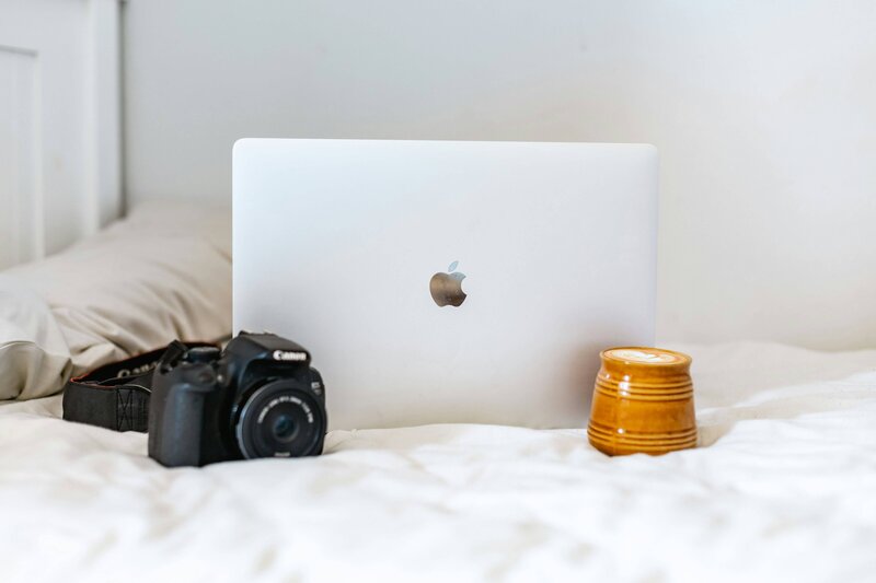 Laptop and camera on a bed, representing the Fix Your Foundations Flow for wedding photographers to simplify and reset workflows.