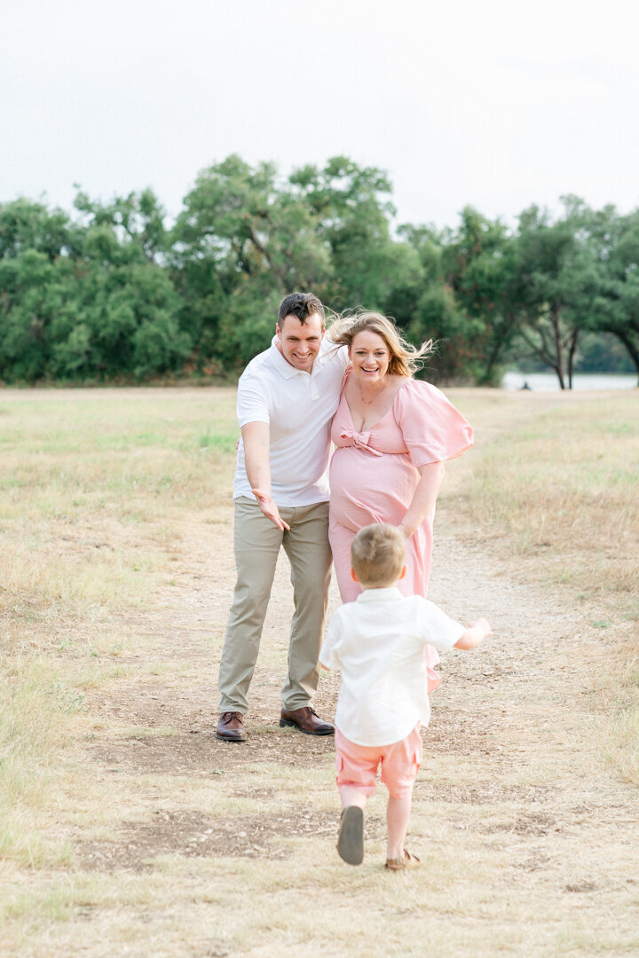 a toddler boy runs towards his mom and dad in this candid photo taken at Brushy Creek Lake Park. 