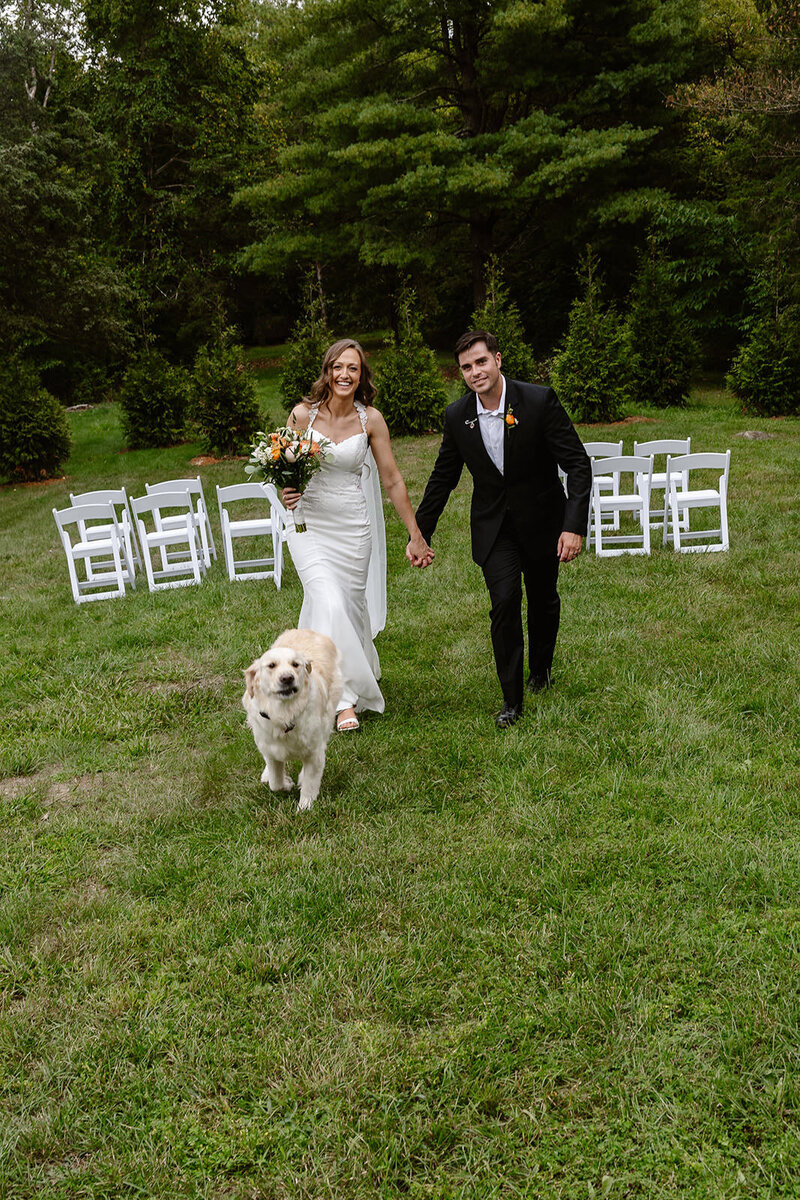A couple holds hands, walking with their dog.