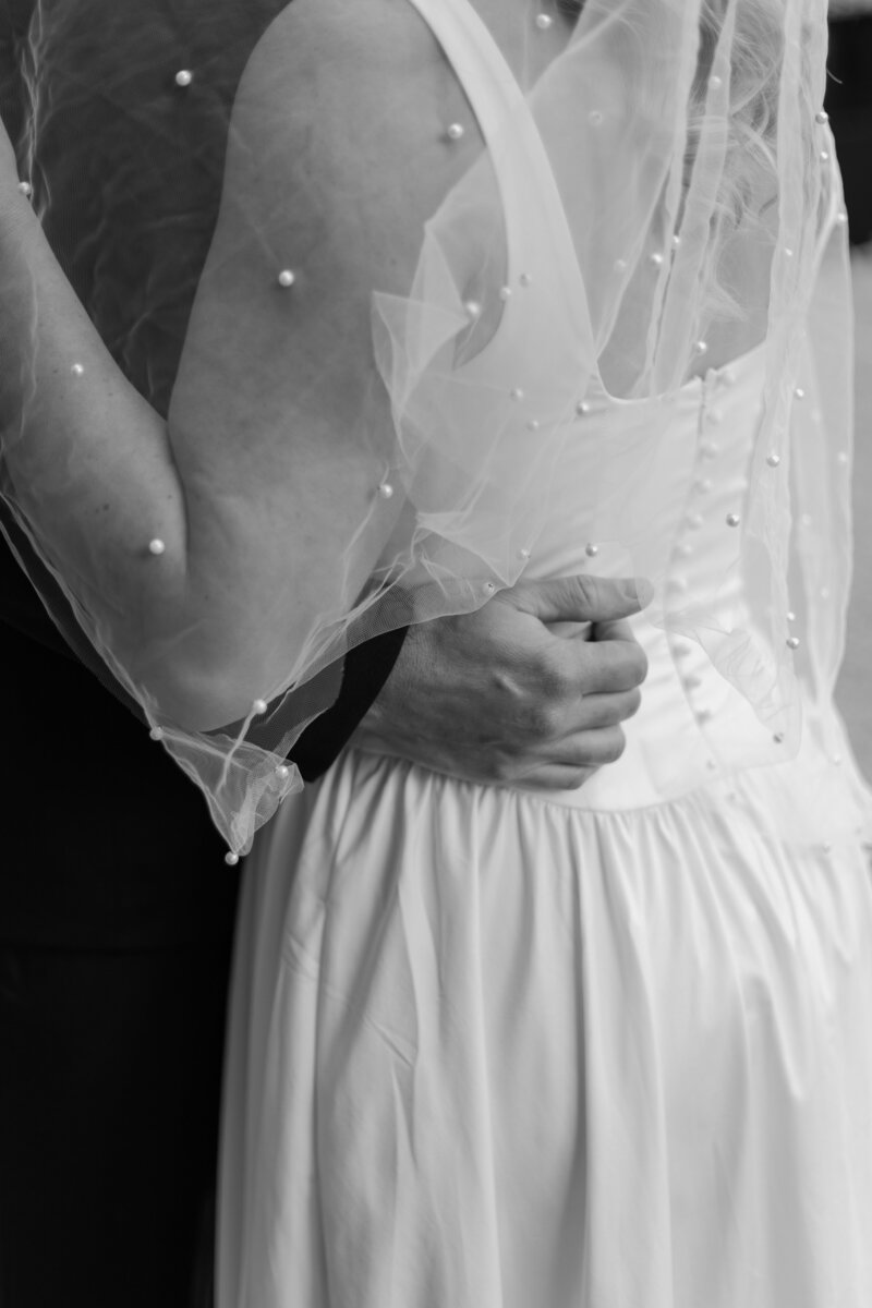 Groom resting hand on bride's waist, in black and white.