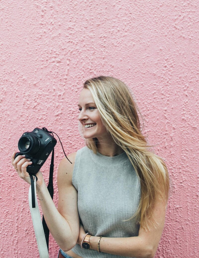Michelle holding a camera against a pink wall