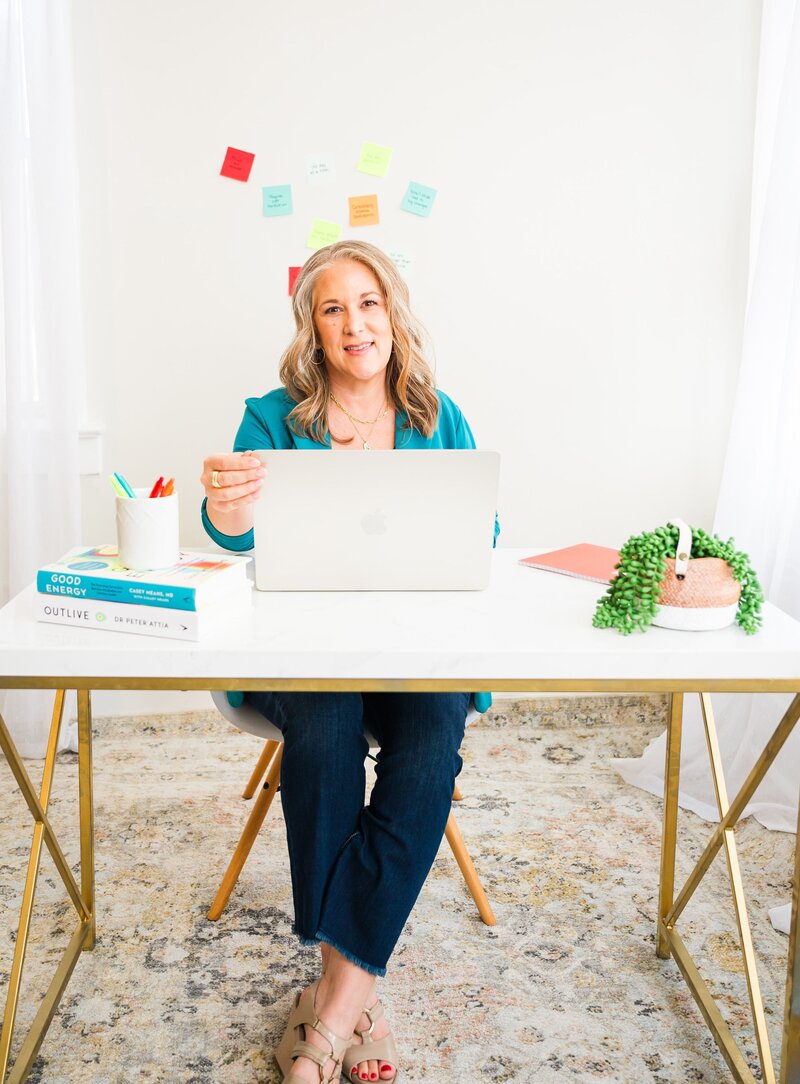 Woman sitting at desk while opening laptop and smiling.