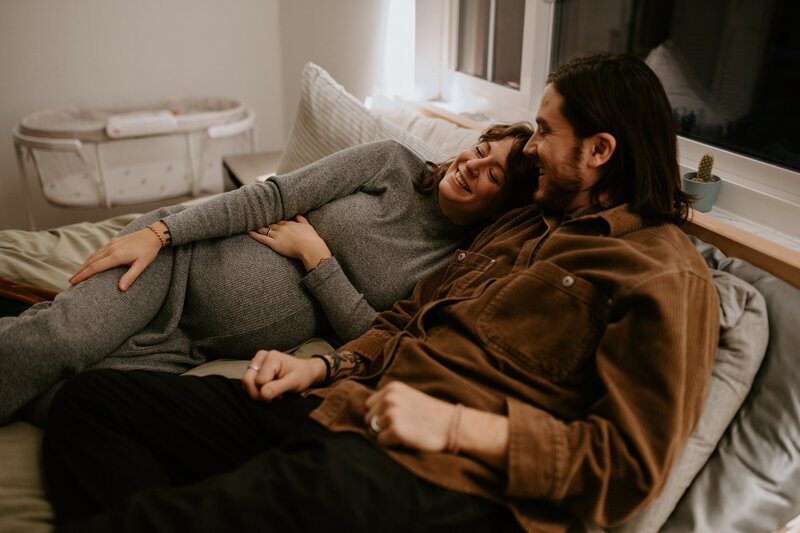 Pregnant couple laughing on a bed in Irvington Indianapolis.