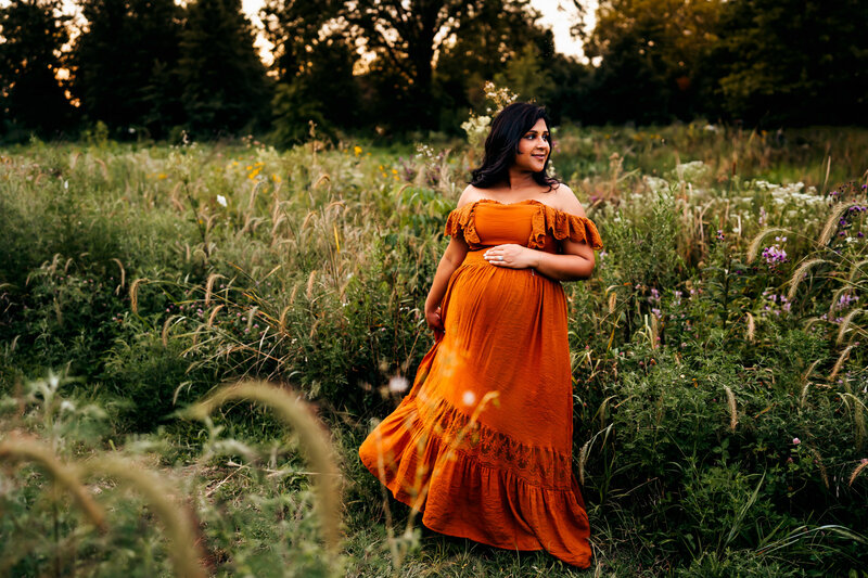 pregnant woman standing in field in oragne dress
