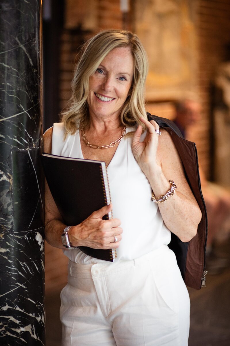Lysanne LaPierre headshot holding a black notebook with a jacket swung over her shoulder