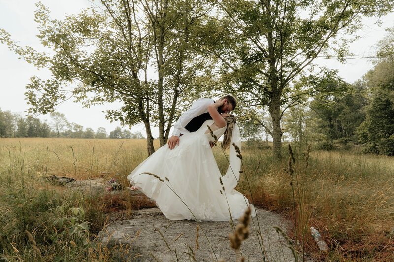 Groom dipping the bride for a kiss in a field.