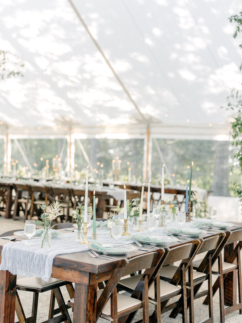 Dark brown wood reception tables and chairs decorated with vases and candles under a clear tent