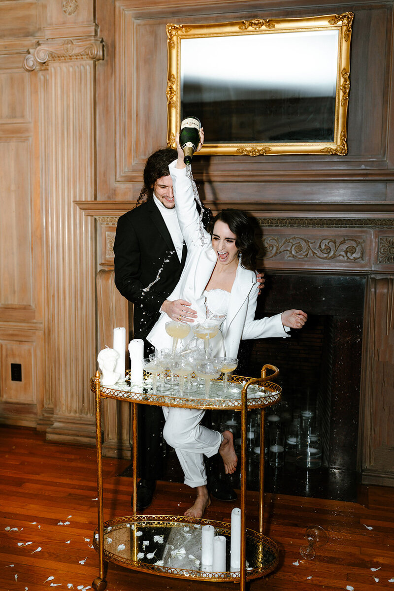 Bride and groom pouring champagne into a tower of glasses while laughing