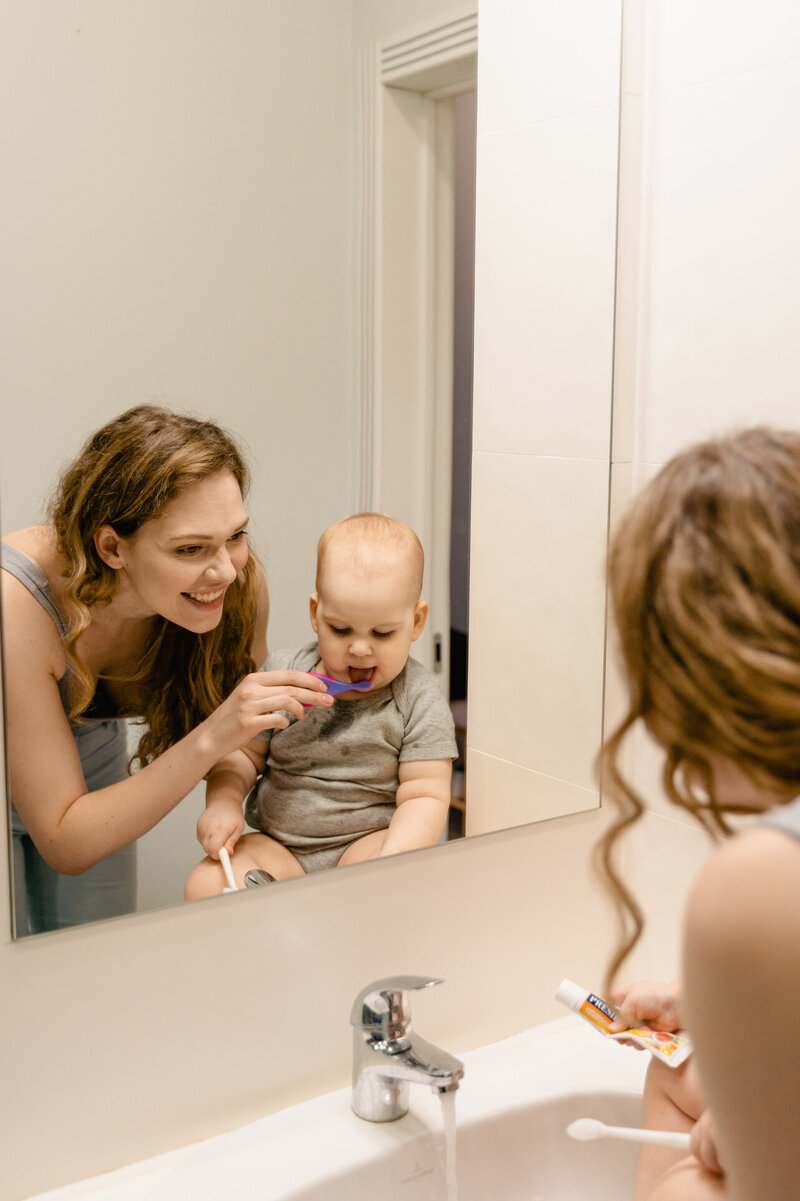 mother brushing her child's teeth with a smile