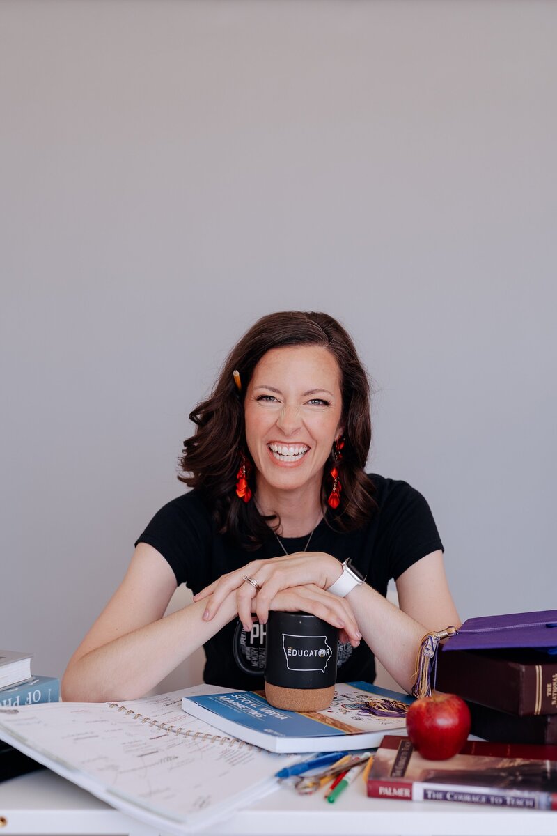 Carrie smiling while sitting at a desk with teaching supplies on it