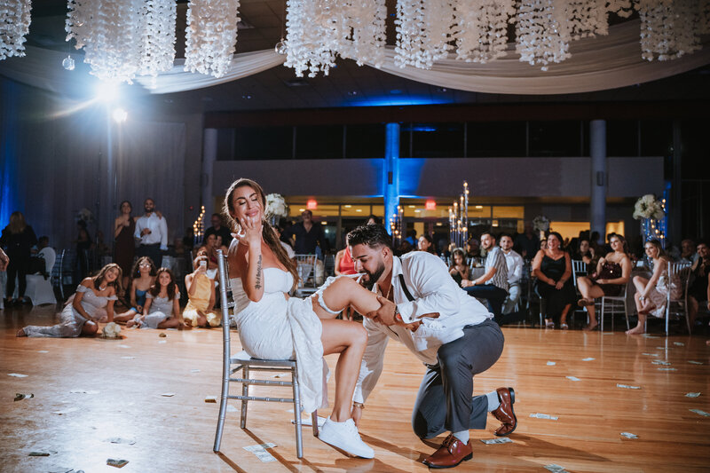 groom taking garter off bride while on the dance floor