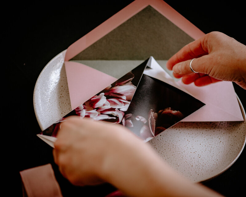 Hands holding a folded origami wedding invitation with pink tulip flowers and pink and green envelope
