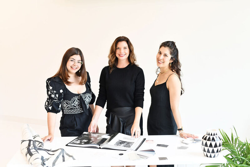 Three interior designers in Lake Norman, NC, collaborating on design plans with samples and an open portfolio book.