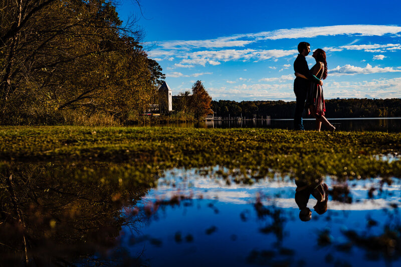 Engagement portrait of a couple at Lake Crabtree Park - they embrace and are also reflected in the water below them