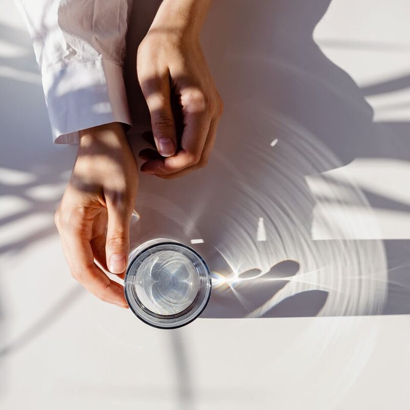 Hands holding a glass of water on top of a white table.