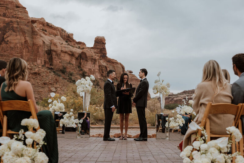 two grooms standing with their officiant at their wedding ceremony in the desert