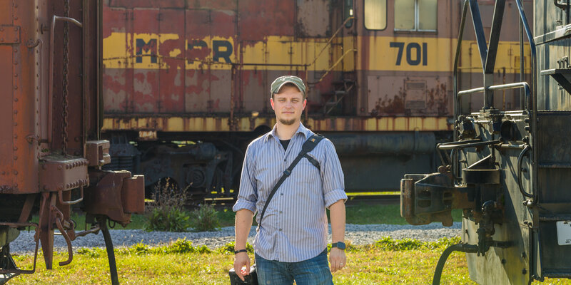 Travis Stitt standing in a train yard during an engagement session, showcasing his creative approach to capturing unique and industrial-inspired moments for engaged couples.