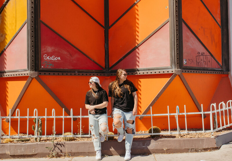 Two people standing in front of a colorful building looking opposite directions.