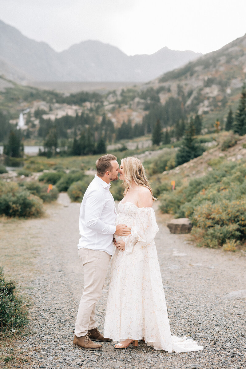 couple kissing expecting their first child in the mountains