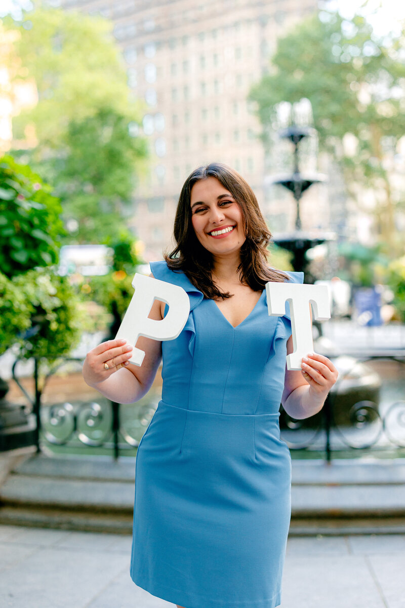 NYU graduate smiling in Madison Square Park while holding white P and T letters.
