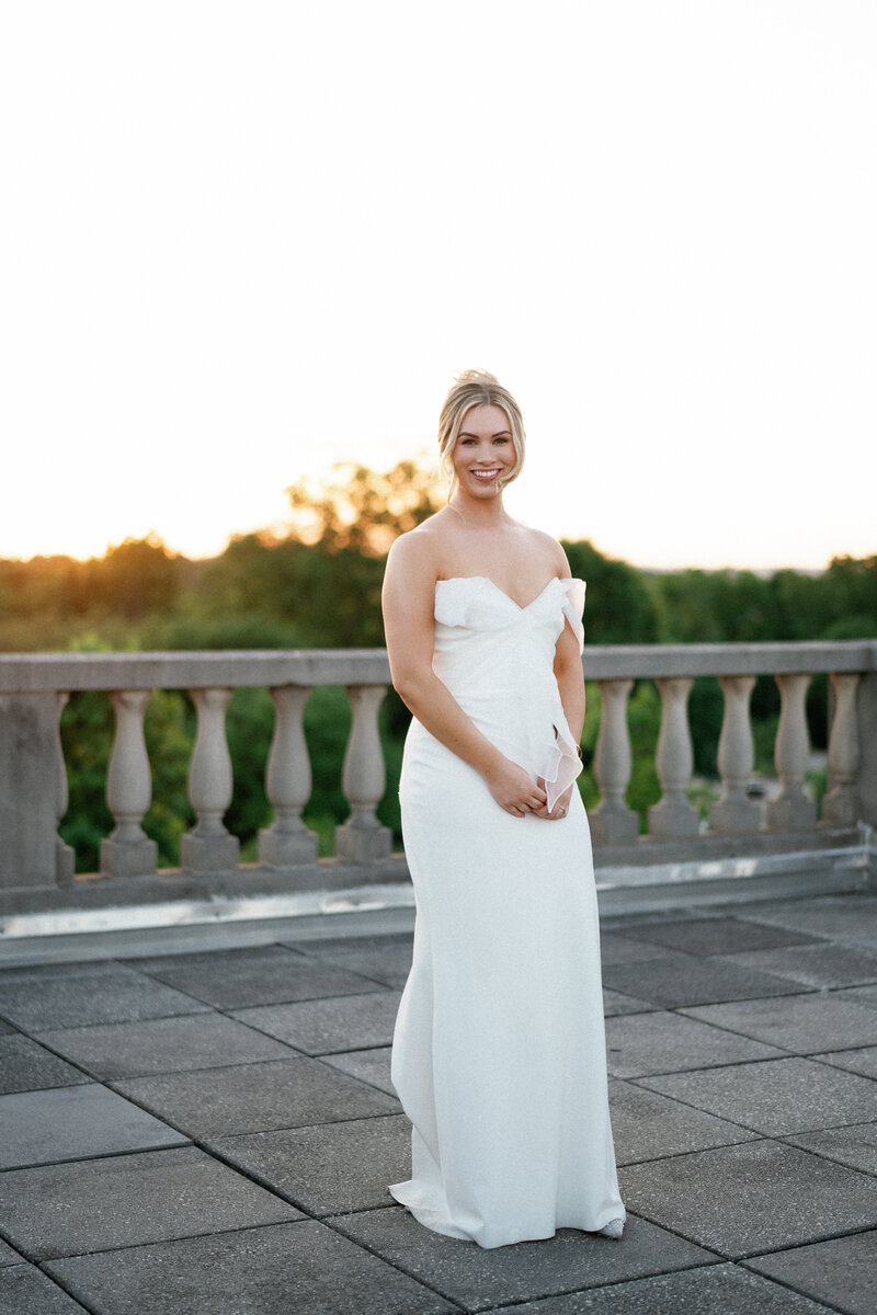 Bride standing alone in strapless gown at sunset on terrace with greenery in the background | Ohio wedding photographer