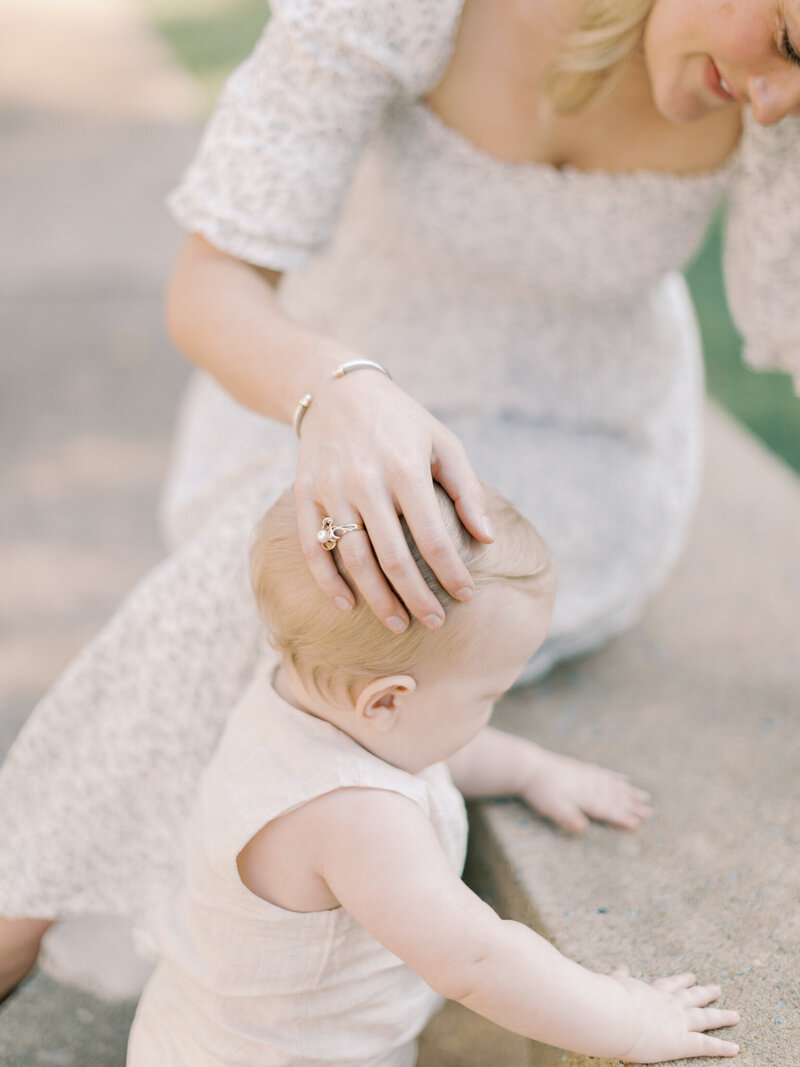 Mother's hand with gold ring caresses one year old son's blonde head  outside of Arkansas State Capitol taken by Little Rock photographer Bailey Feeler