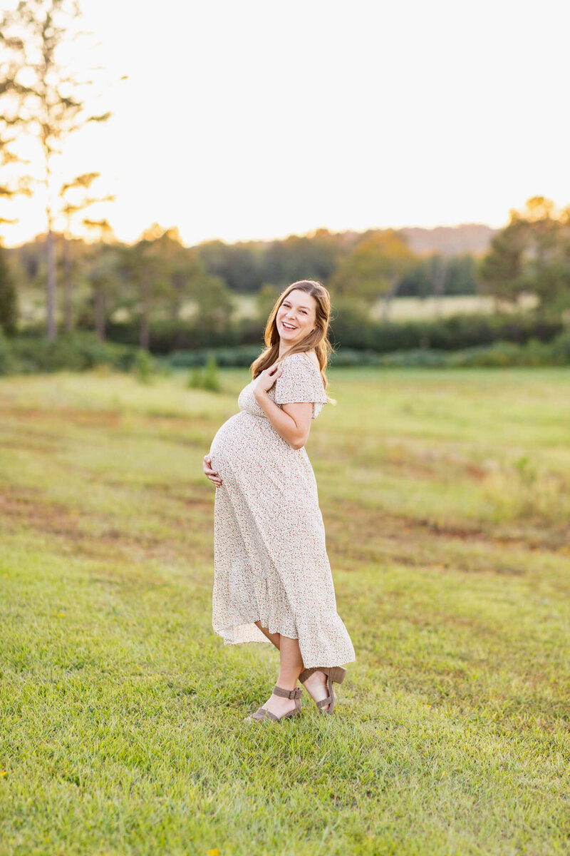 Expectant mom in a cream dress sitting on a bed and holding her belly