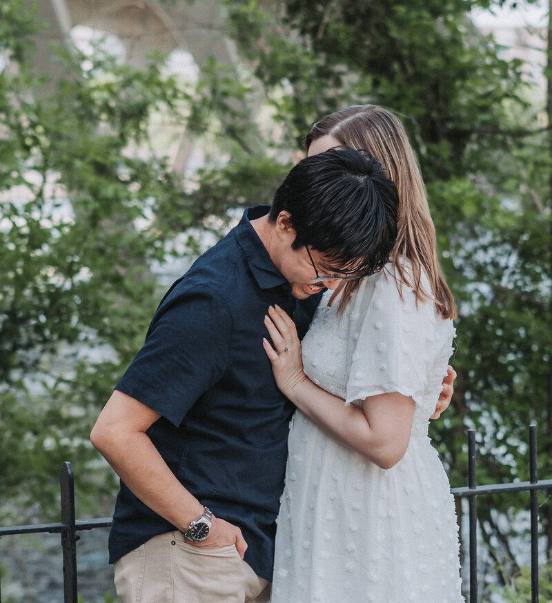 A candid and affectionate moment captured between a couple on Brown's Island in Richmond, Virginia, with lush greenery and a bridge in the background, perfect for an engagement session by Quinn Photography LLC.