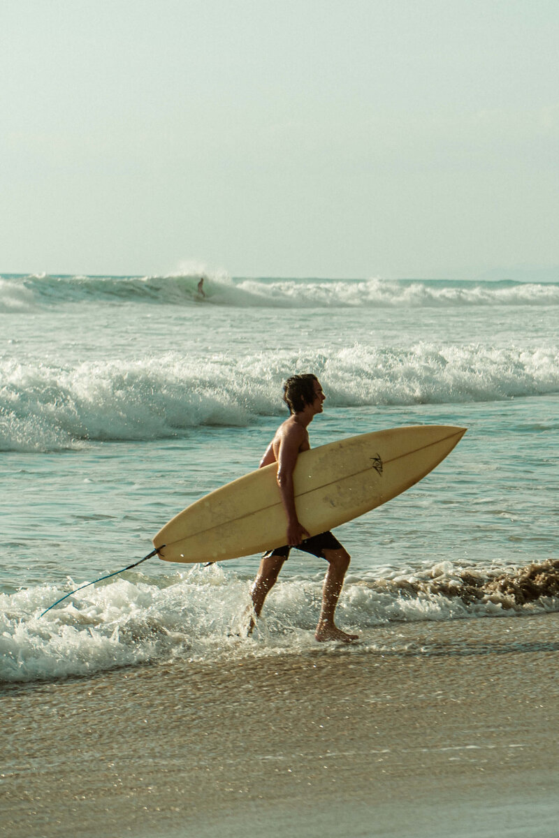 Man coming out of the ocean holding a surf board