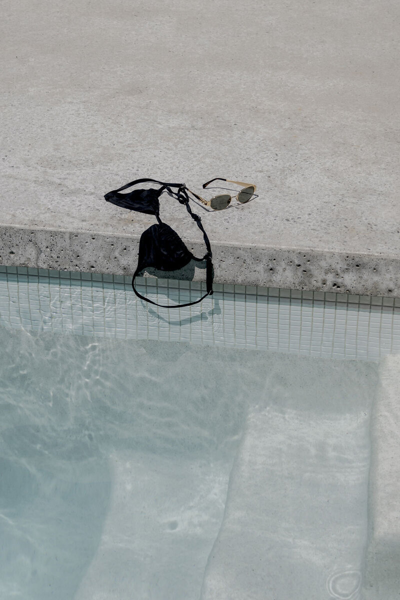 Black bikini and sunglasses placed on the edge of a swimming pool with blue water, used for Everwell Pilates case study