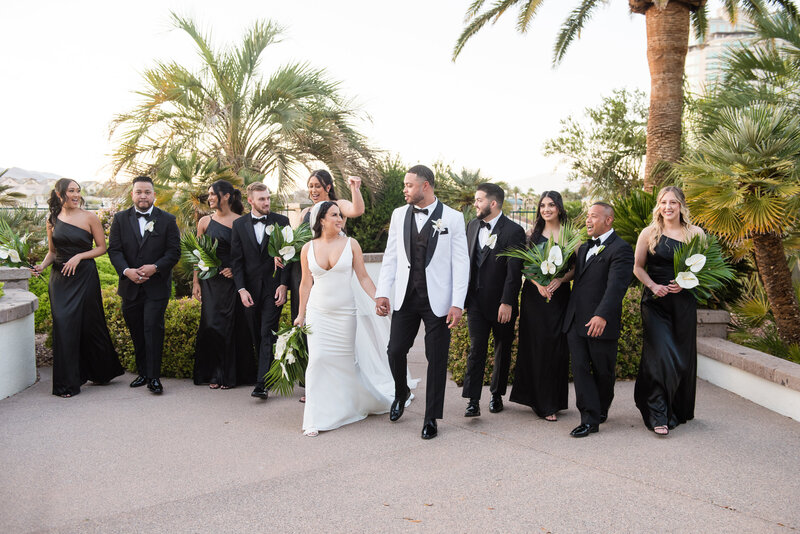 Bridal party in black and white attire posing with the couple in the lush courtyard.