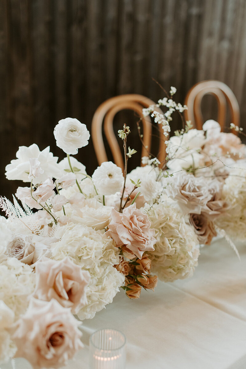 Close-up of reception table with white hydrangea, neutral roses, and bleached fern in lucite vases, styled with candlelight at Jenay and Daniel’s wedding by Summer Robbins Flowers in Central Oregon