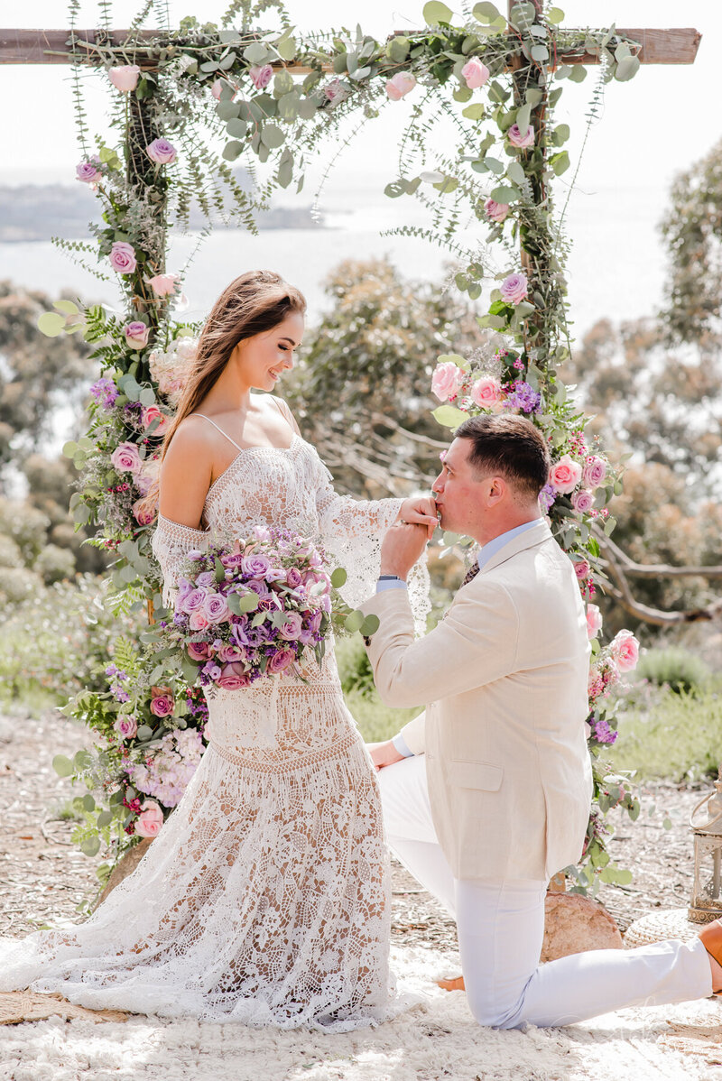 groom on one knee kissing his bride's hand at la jolla